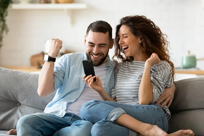 man-and-woman-couple-on-couch-excited-reading-phone