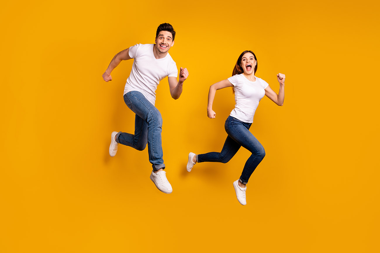 Man and woman smiling, jumping while running on yellow background