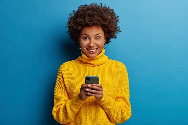 woman-holding-phone-wearing-yellow-knit-sweater