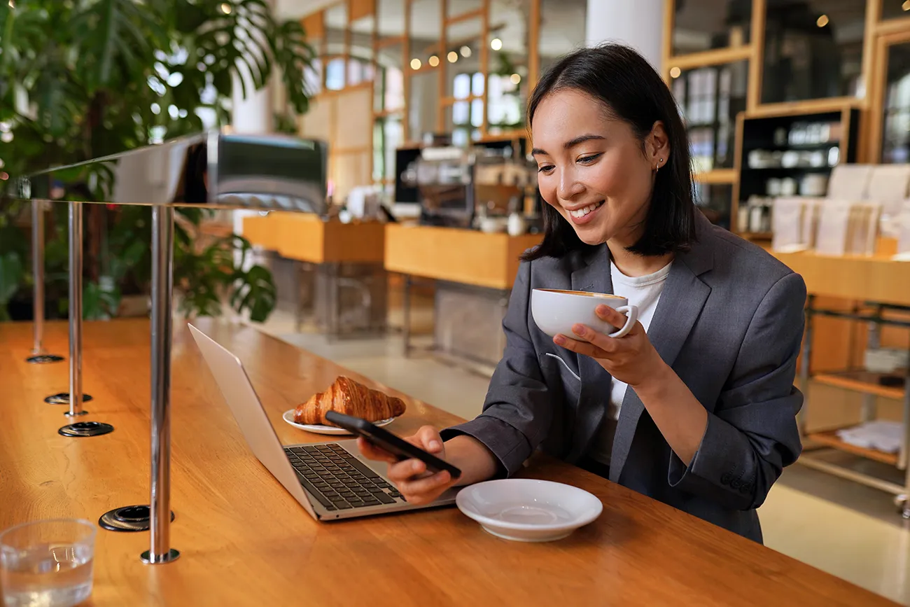 woman-using-phone-and-computer-in-coffee-shop