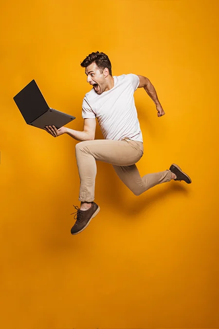 excited man jumping for joy holding computer